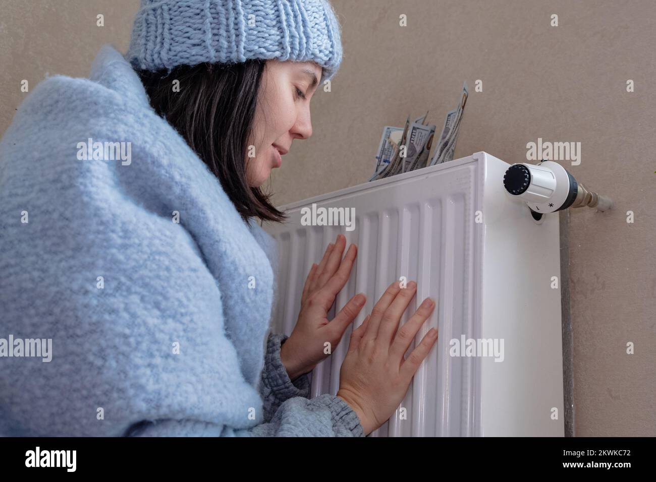 Die Hitze wird teurer, eine Frau wärmt ihre Hände am Heizkörper Stockfoto
