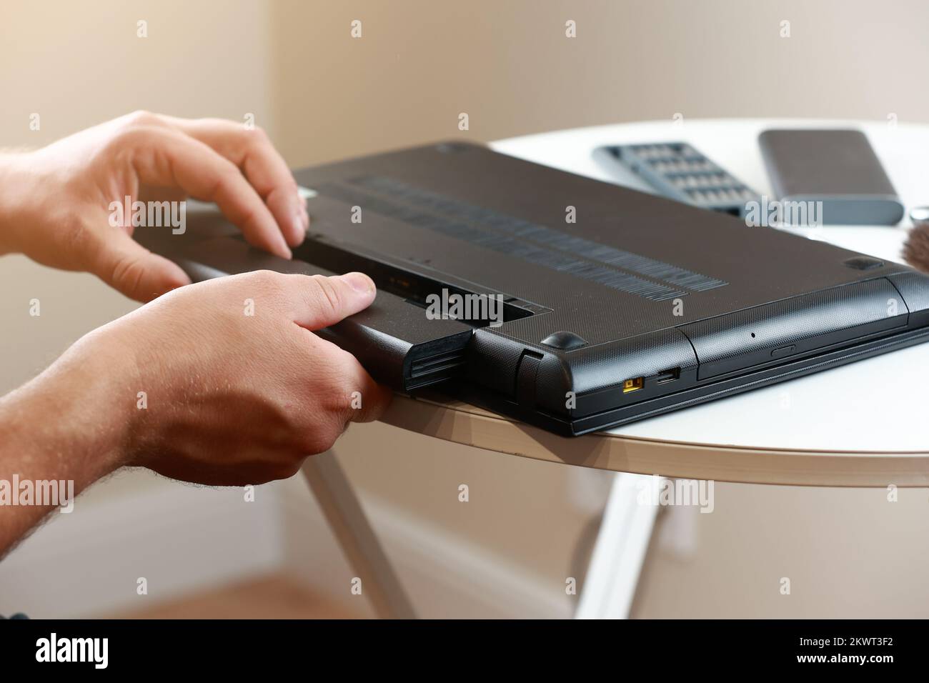 Die Hände des Reparaturmanns, der den Akku aus dem Laptop entfernt ...