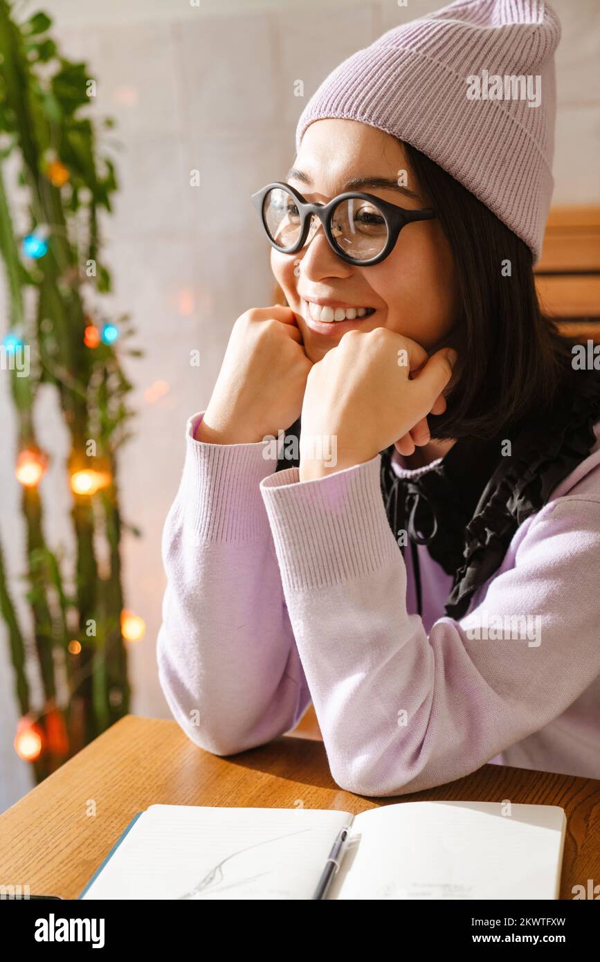 Junge Asiatin mit Brille, die lächelt, während sie im Café sitzt Stockfoto