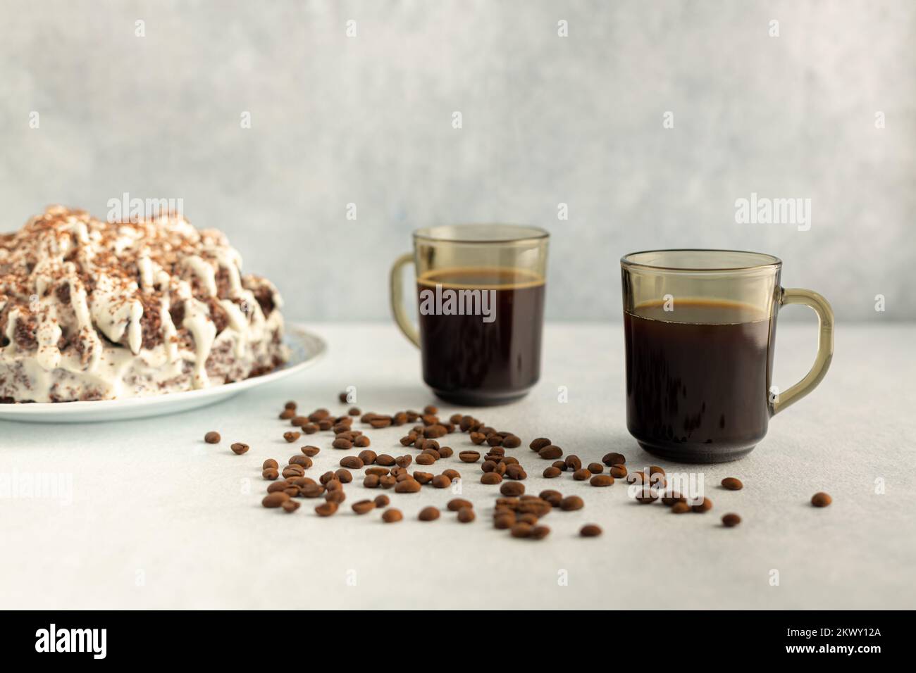 Kaffee in einer Glaskanne mit Kaffeebohnen, Sahnetorte. Trinken Sie auf hellgrauem Hintergrund. Stockfoto