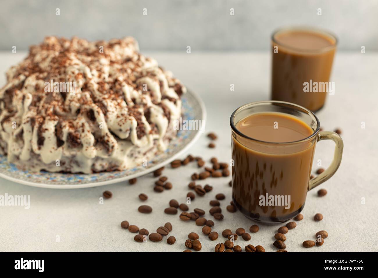 Kaffee mit Rahm in einem Glas Becher mit Kaffeebohnen, Sahnetorte. Trinken Sie auf hellgrauem Hintergrund. Stockfoto