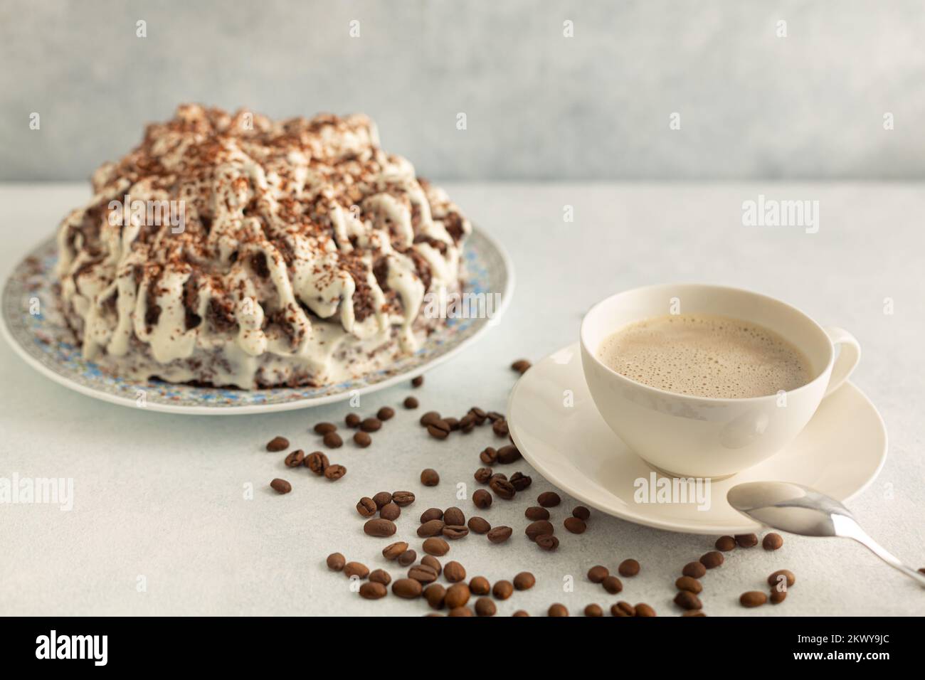 Kaffee mit Creme in einem weißen Set mit Kaffeebohnen, Sahnetorte. Trinken Sie auf hellgrauem Hintergrund. Stockfoto