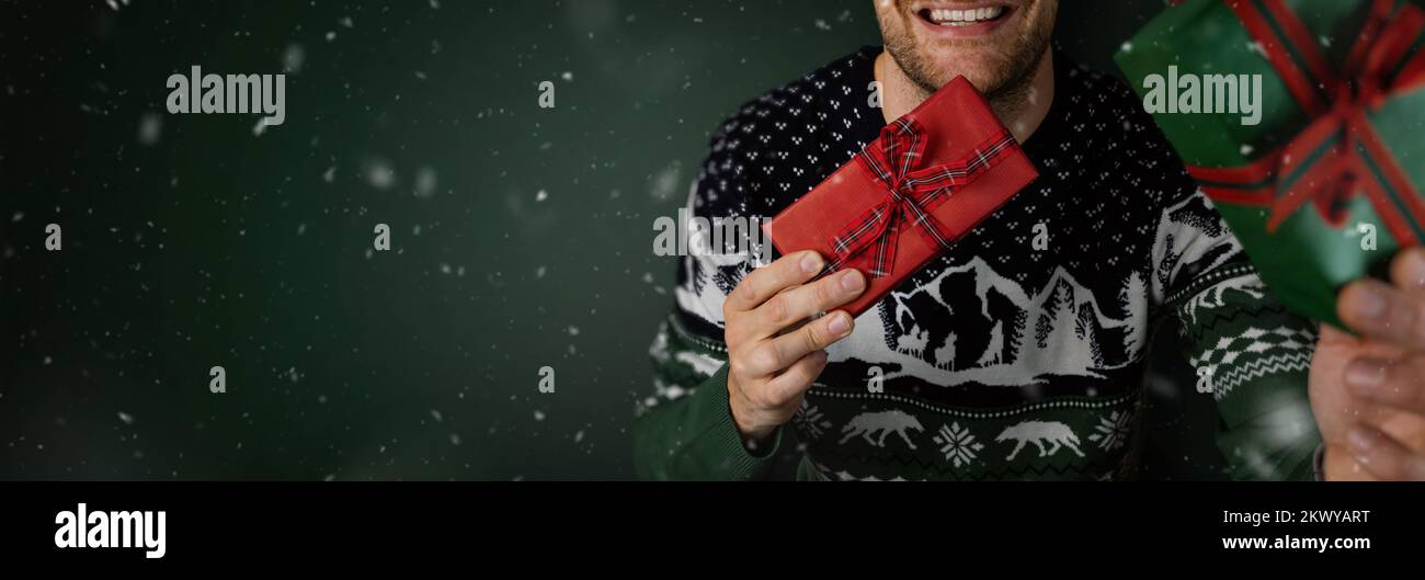 Lächelnder Mann im weihnachtspullover mit Geschenkschachteln auf grünem Hintergrund. Banner mit Kopierbereich Stockfoto