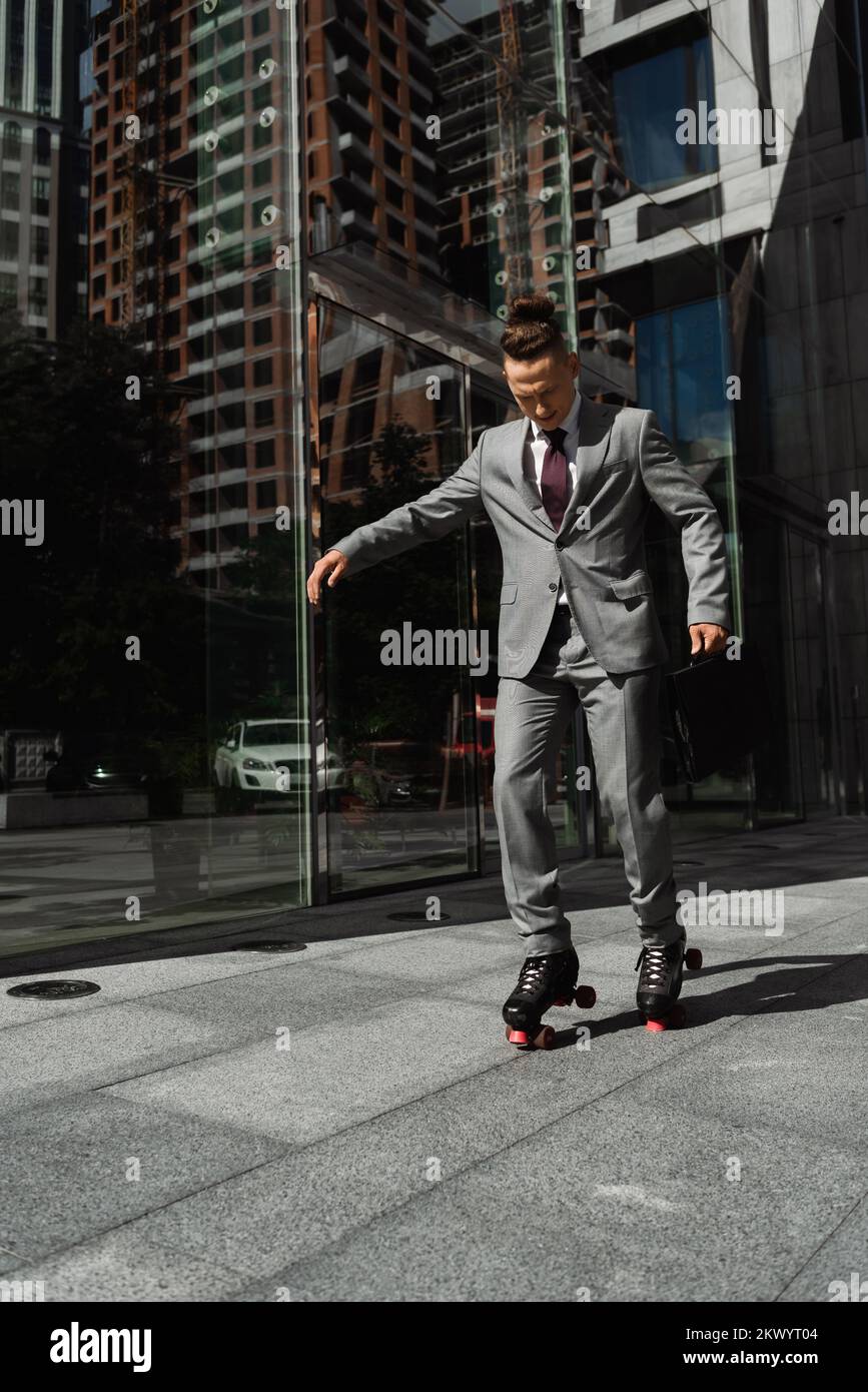Langer junger Geschäftsmann mit trendigen, haarsträubenden Rollschuhlaufen auf der City Street, Bild der Börse Stockfoto