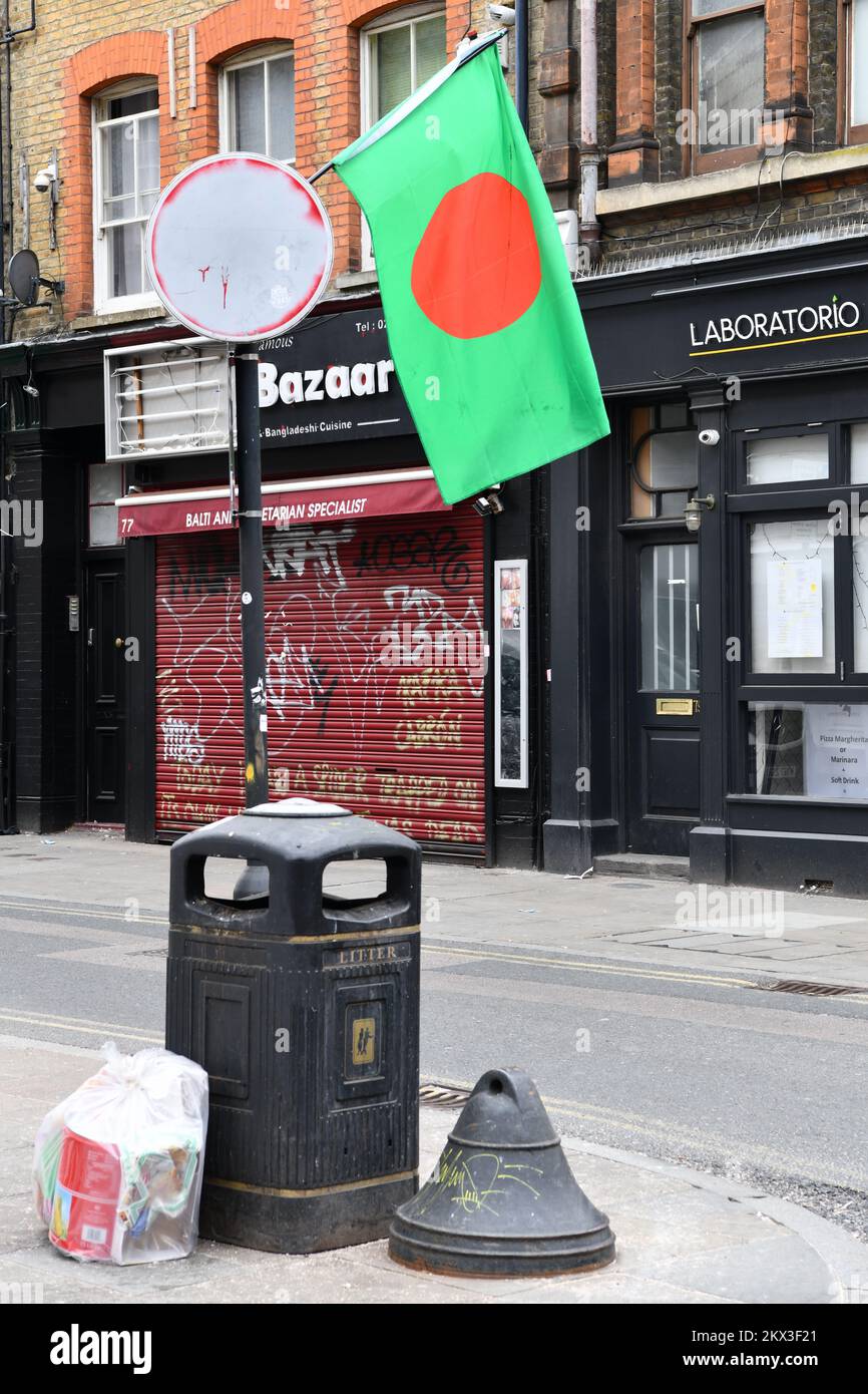 Bangladesch Nationalflagge, die von einem übermalten Straßenschild über einem Mülleimer auf Brick Lane Shoreditch London fliegt Stockfoto