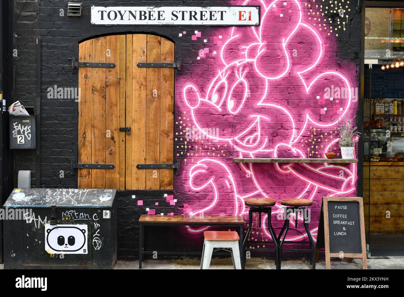 Sitzecke im Freien außerhalb des Cafés in der Toynbee Street Spitalfields London mit Straßenkunstkulisse von Minnie Mouse Stockfoto