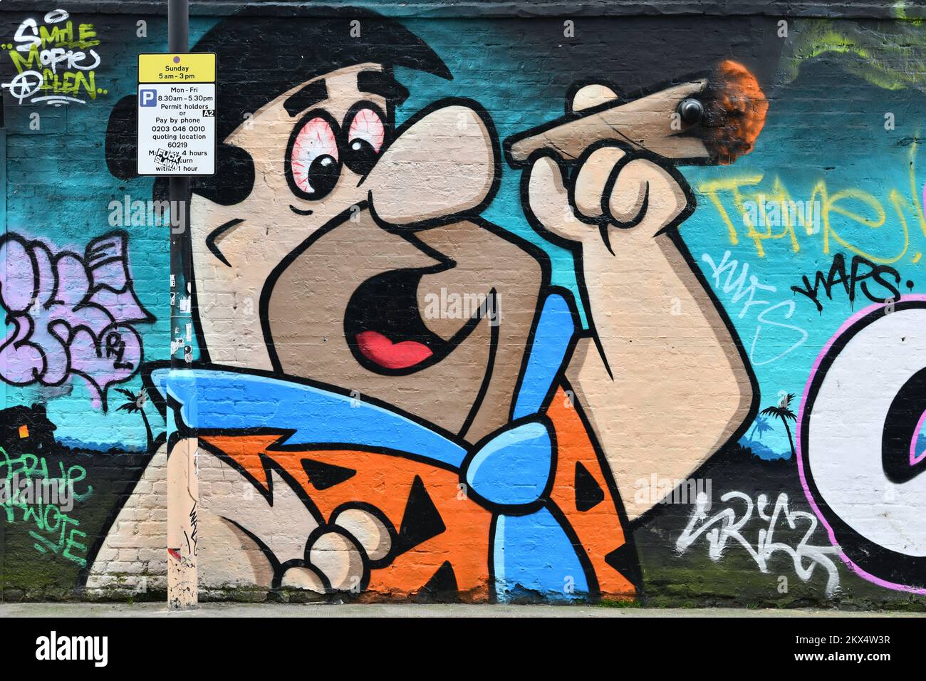 Parkplatzinformation Schild an der Laterne vor Fred Flintstone raucht eine verzweigte Straßenkunst in Shoreditch London Stockfoto