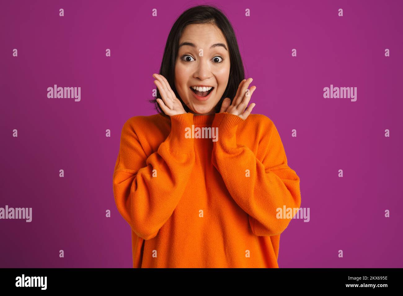 Junge asiatische Frau, die sich vor der Kamera über lila Hintergrund überrascht Stockfoto