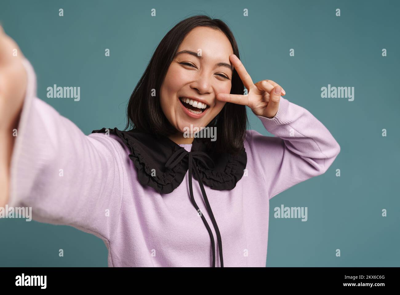 Junge asiatische Frau, die beim Selfie-Fotografieren isoliert auf blauem Hintergrund Gesten macht Stockfoto