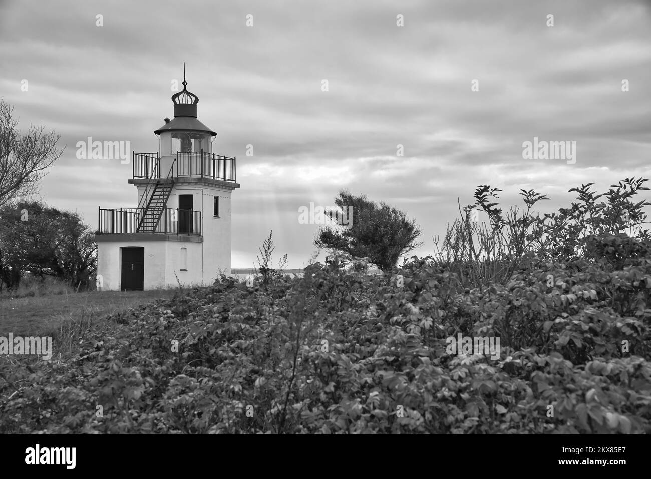 Schwarzweißer Leuchtturm, Spodsbjerg Fyr in Huntsted an der Küste Dänemarks. Die Sonne scheint durch die Wolken. Wiese mit Bäumen. La Stockfoto