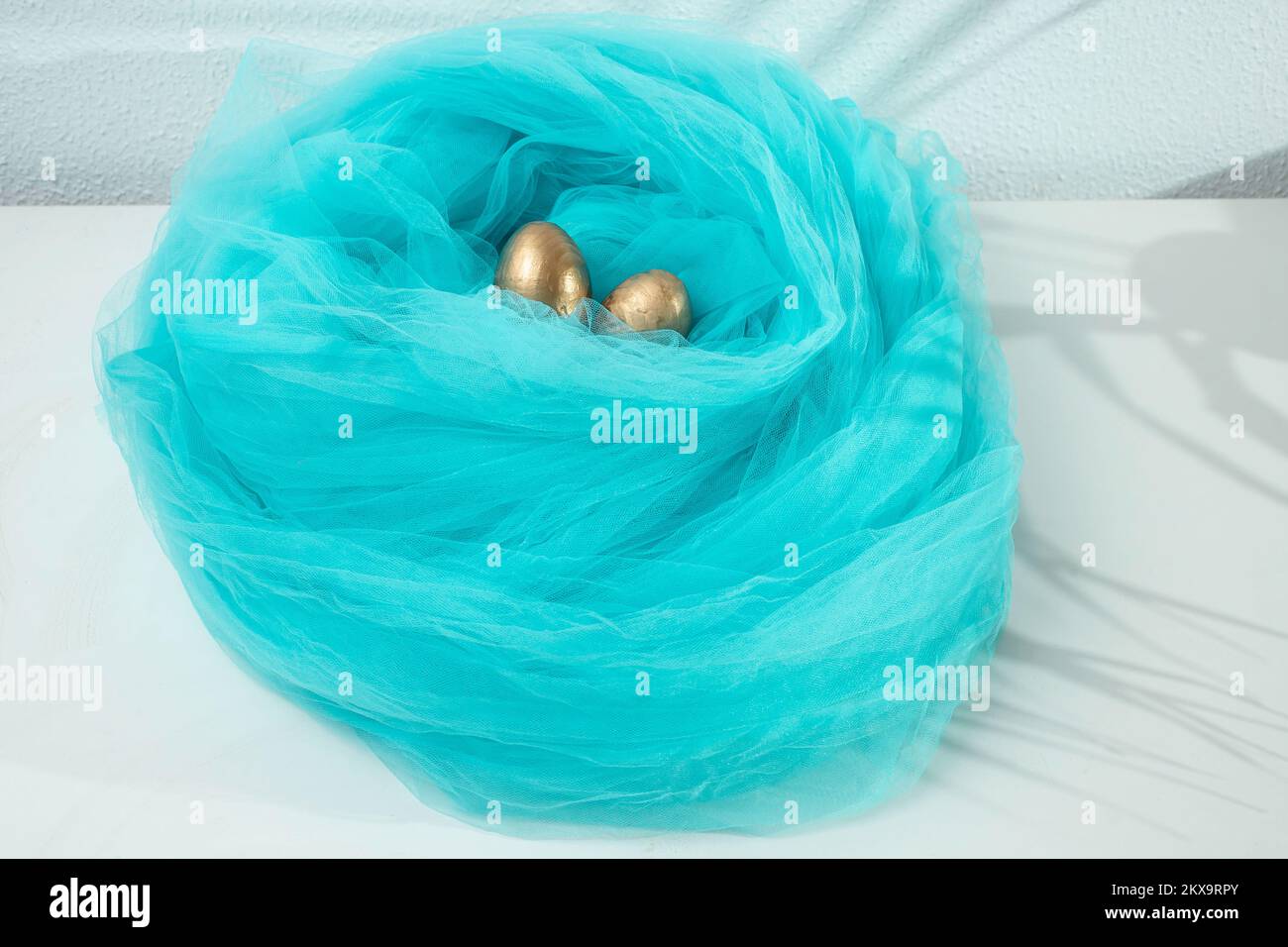 Goldene Eier in einem blauen Stoffnest auf weißem Hintergrund Stockfoto