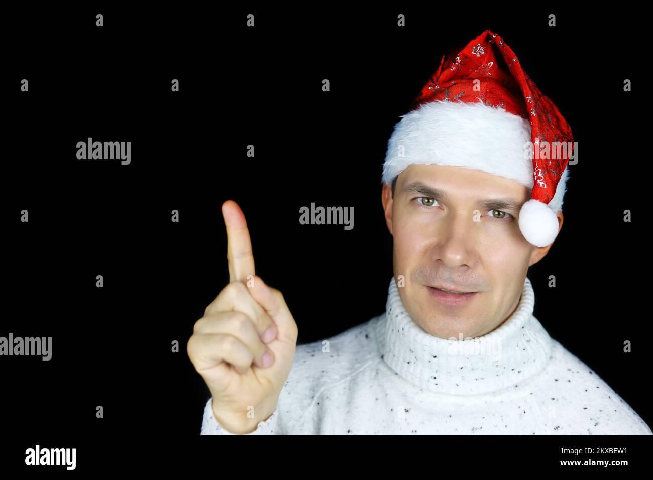 Porträt eines glücklichen Mannes mit Weihnachtsmannmütze, der mit dem Finger auf schwarzem Hintergrund nach oben zeigt. Weihnachtsfeier, Neujahrsfeier Stockfoto