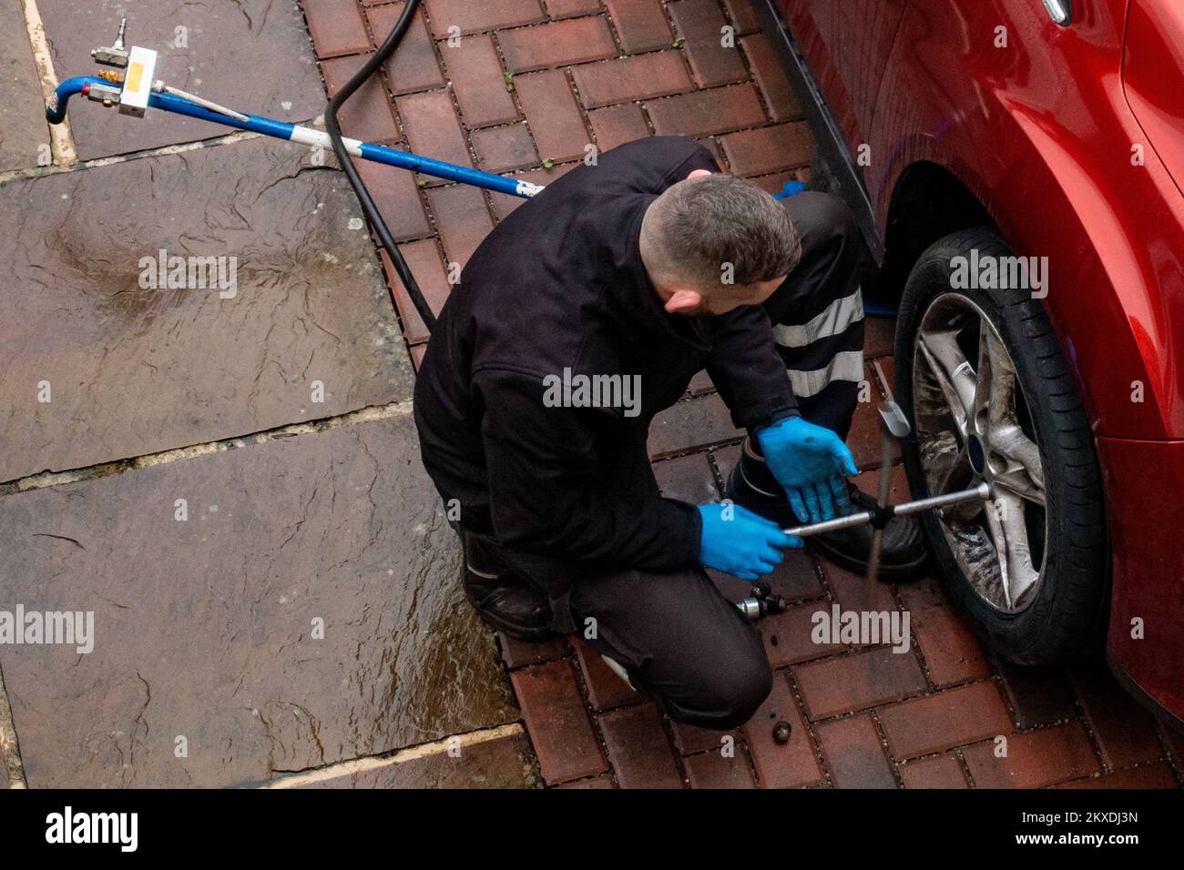 Mechaniker wechselt Autoreifen, während der Reparatur eines Punkts in der Einfahrt, Großbritannien Stockfoto