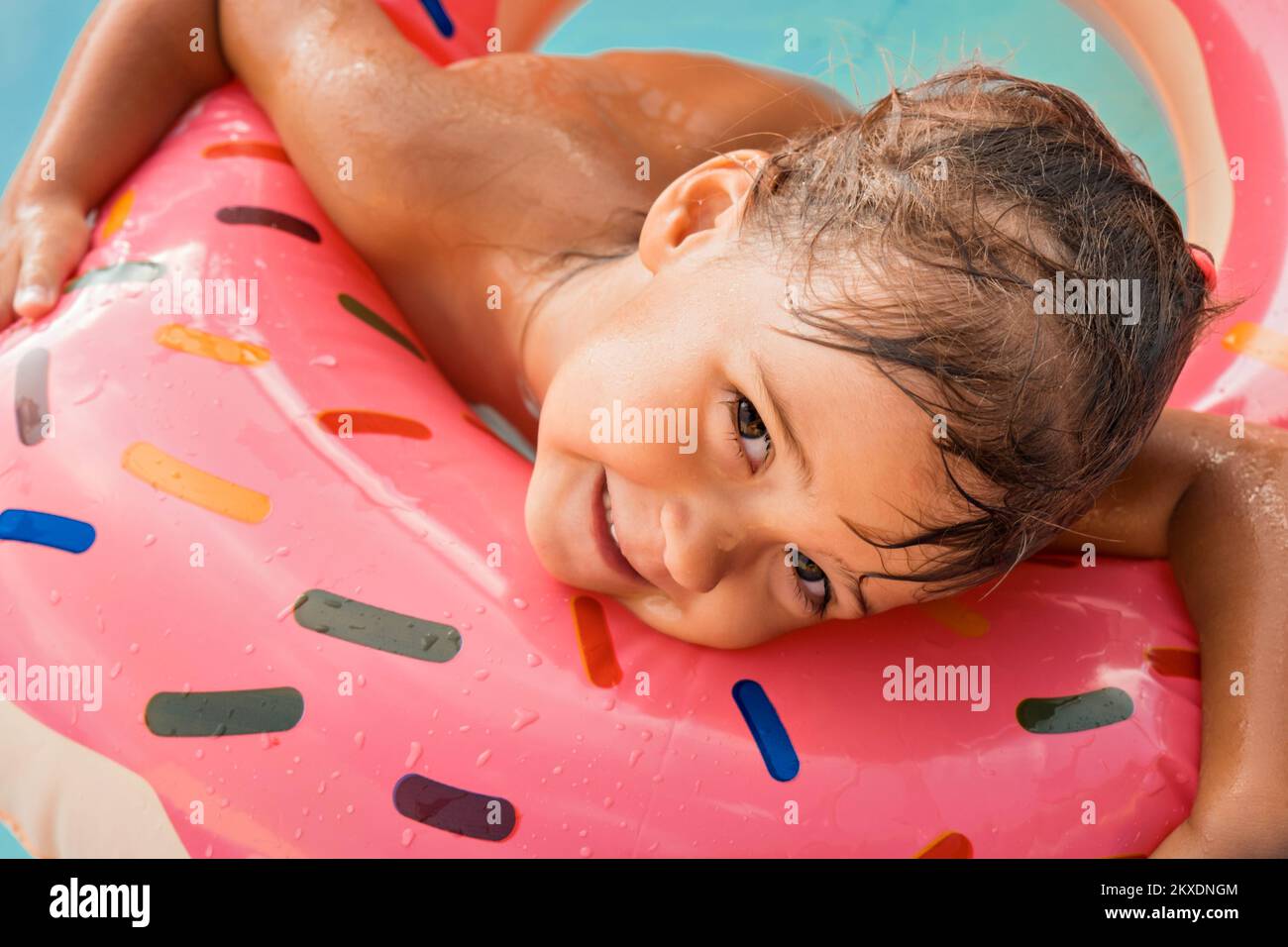 Ein europäisches Mädchen badet in einem blauen Pool in einem rosa großen Gummiring. Nasses Haar und ein fröhliches Lächeln. Wellen, Hotel und Strand. Die Familie genießt einen schönen Urlaub. Hochwertiges Foto. Stockfoto