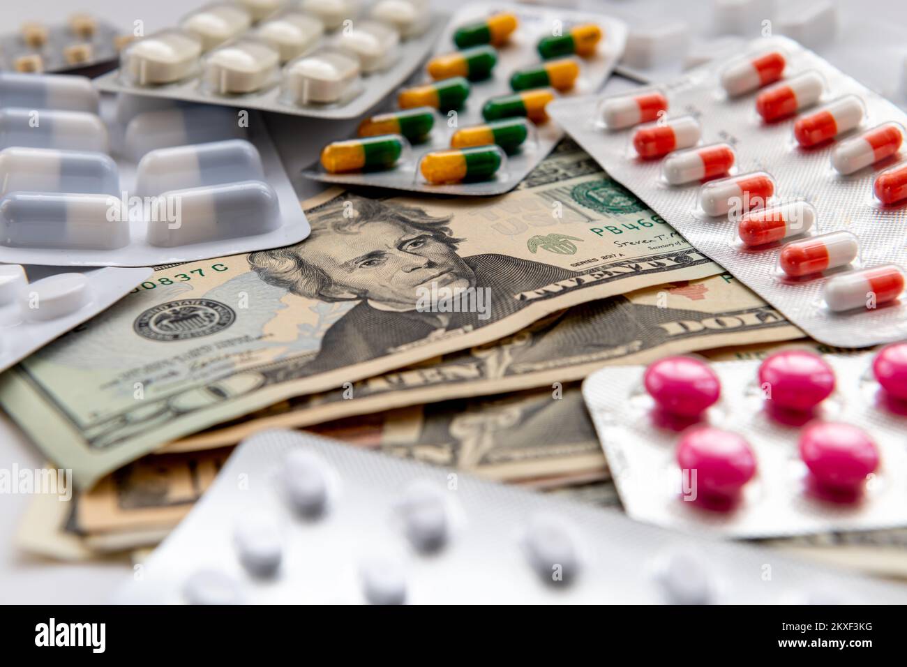 Eine Auswahl an Medikamenten, die auf einem Haufen US-Dollar-Scheine verstreut sind. Medizinische Kosten, großes Pharmakonzept. Stockfoto