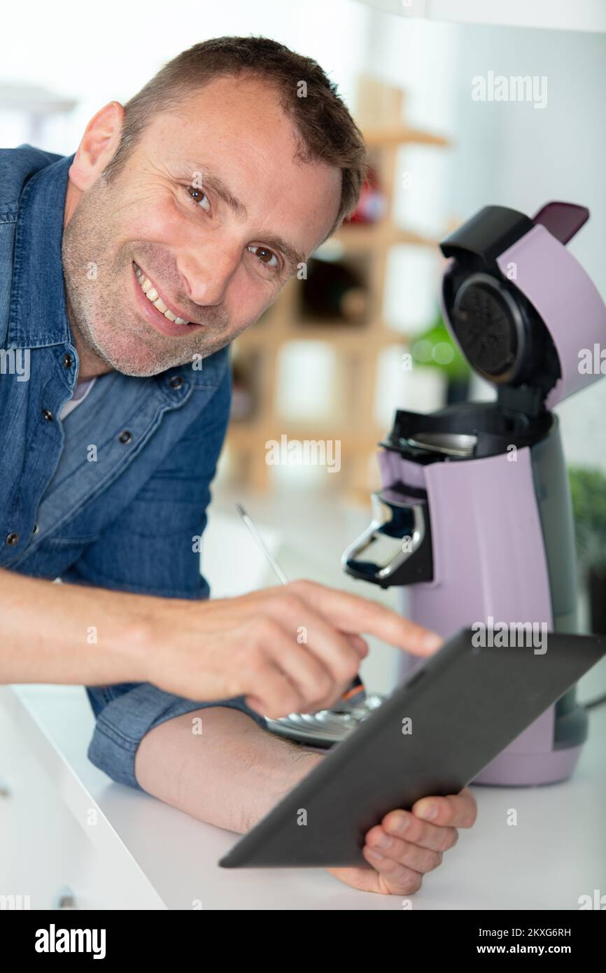 Mann, der beim Reparieren einer Kaffeemaschine auf dem Tablet nachsieht Stockfoto