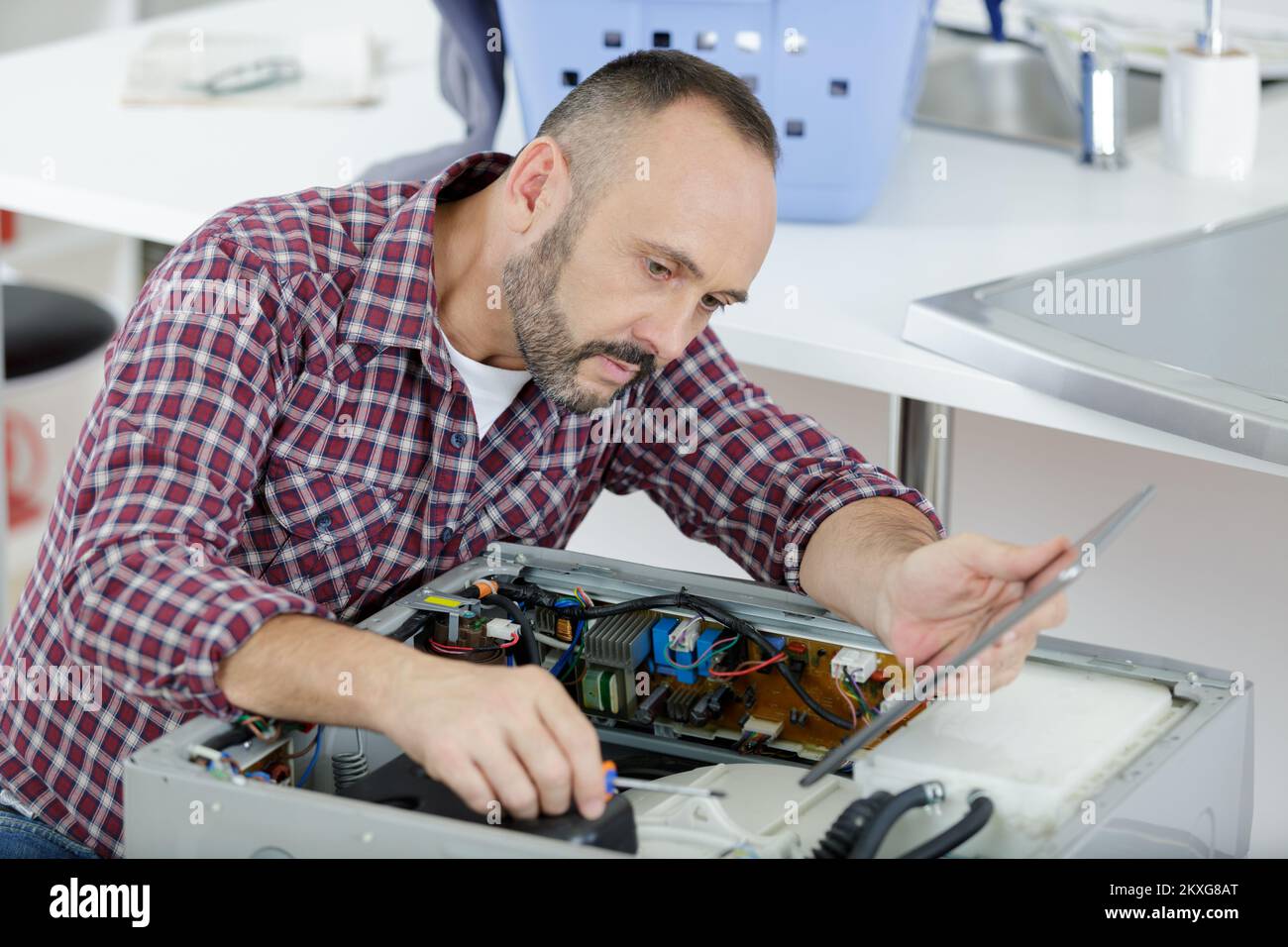 Erfahrener Servicemitarbeiter, der an der Appliance arbeitet und ein Tablet hält Stockfoto