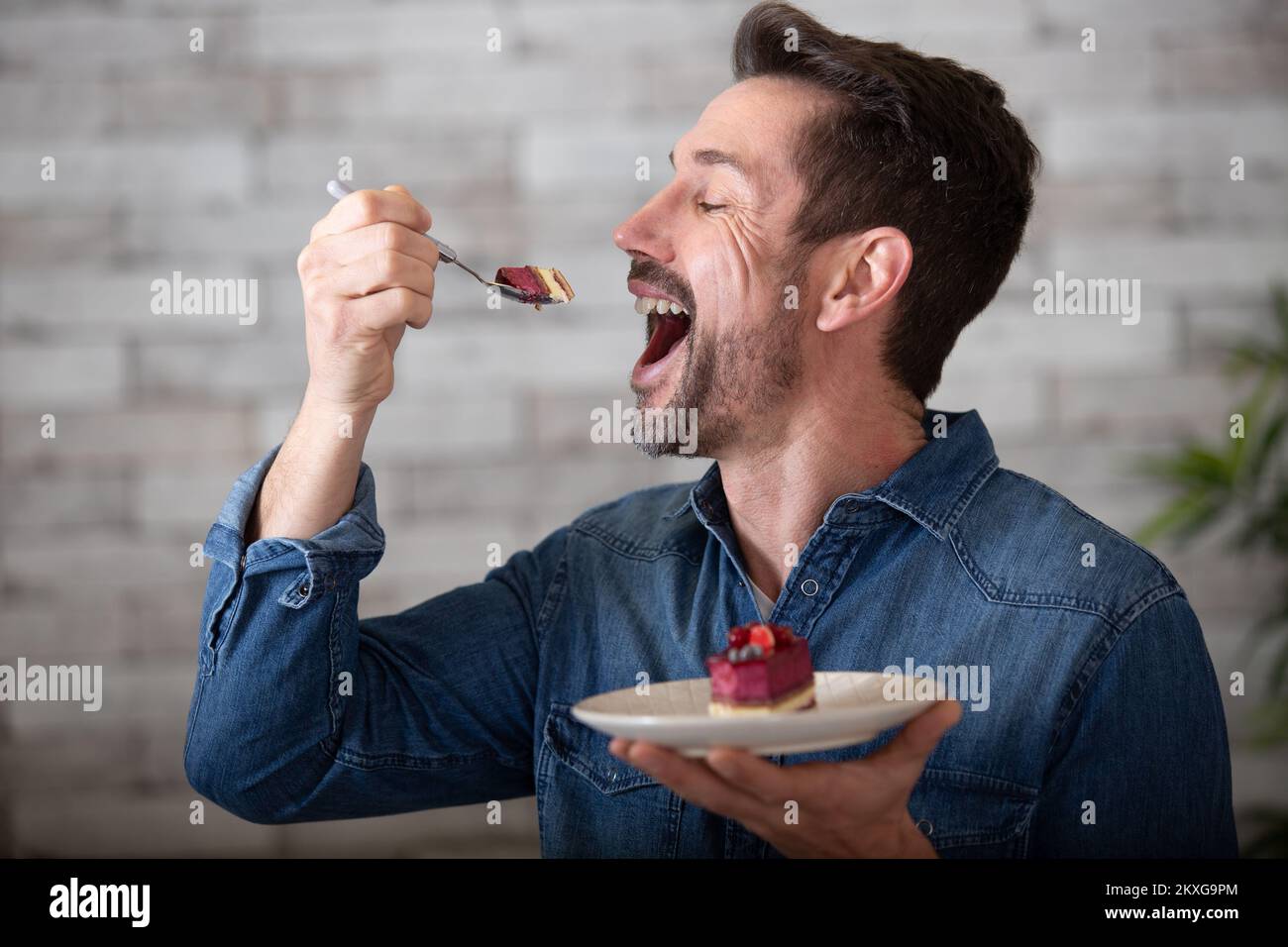 Ein fröhlicher Mann, der einen Mund voll Kuchen nimmt Stockfoto