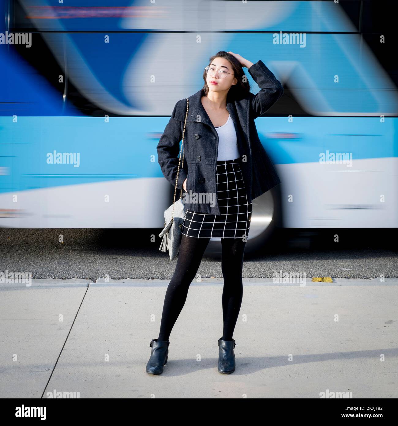 Junge Frau in legerer Business-Kleidung, die auf dem Bürgersteig der Stadt steht, mit schnellem Busverkehr im Hintergrund verschwommen Stockfoto