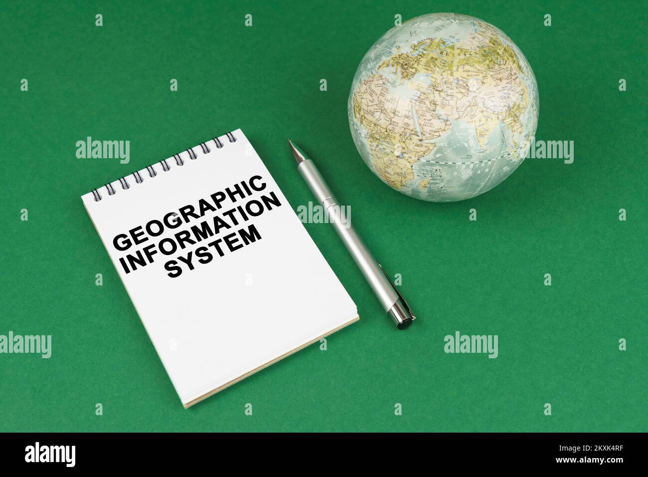 Globales Konzept. Auf einer grünen Oberfläche liegt ein Modell des Planeten und ein Notizblock mit der Aufschrift Geographisches Informationssystem Stockfoto