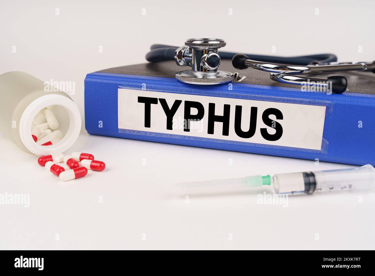 Medizinisches Konzept. Auf einer weißen Oberfläche sind Pillen, eine Spritze, ein Stethoskop und eine Mappe mit der Inschrift - Typhus Stockfoto