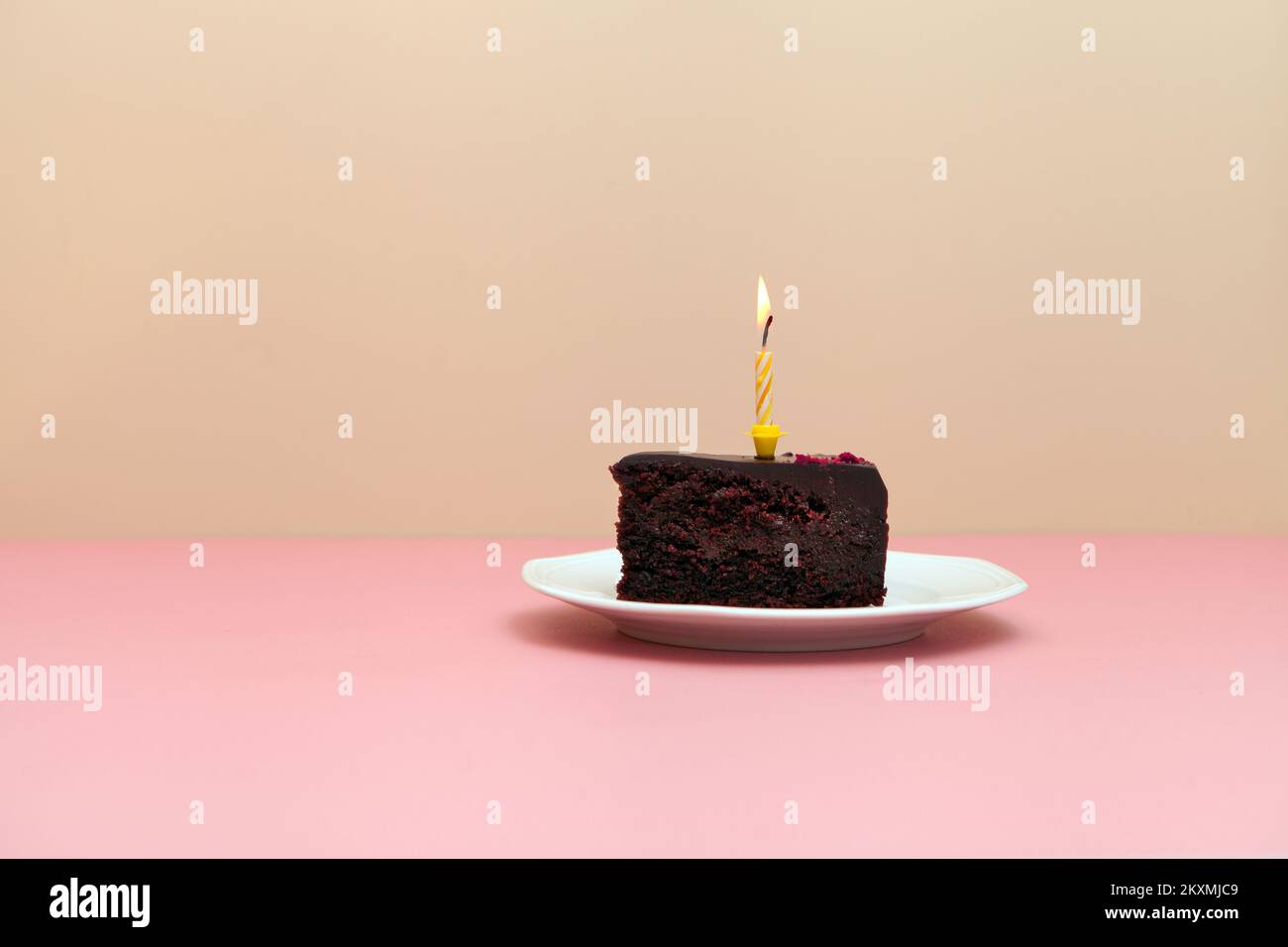 Schokoladenkuchen mit brennender Kerze auf rosa Hintergrund. Happy Birthday Torte or Pie - minimalistisches Bild Stockfoto