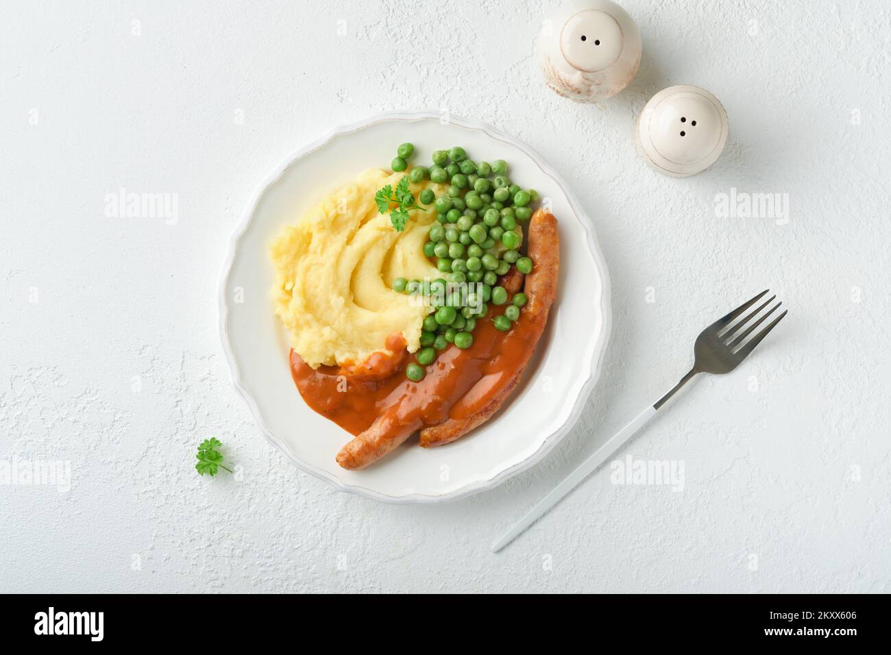 Knaller und Püree. Gegrillte Würstchen mit Kartoffelpüree und grüner Erbse auf weißem Teller auf hellem Hintergrund. Traditionelles Gericht aus Großbritannien und Irland. B Stockfoto