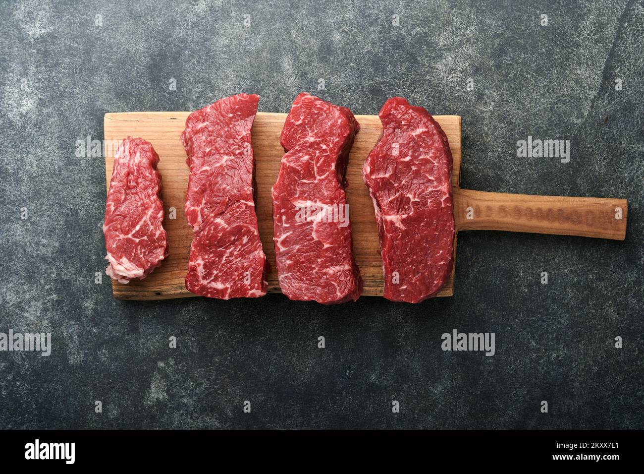 Rohe Steaks. Top Blade Steaks auf Holzbrettern mit Gewürzen, Rosmarin, Gemüse und Zutaten zum Kochen auf schwarzem Hintergrund. Draufsicht. Kopieren en Stockfoto