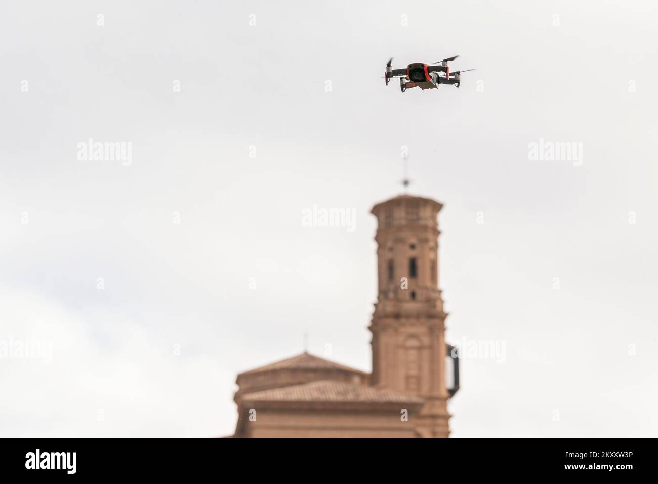 Video-aufzeichnende Quadcopter-Drohne, die in einem klaren Himmel in der Nähe einer Kirche fliegt Stockfoto