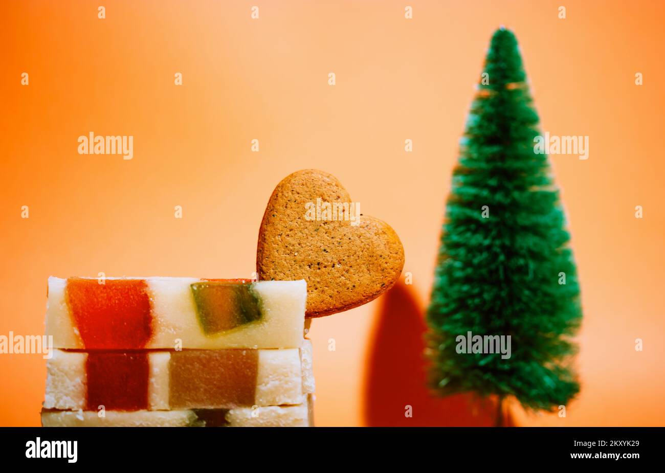 Marzipan-Marmeladen-Turrone auf orangefarbenem Hintergrund. Spanisches Dessert aus Mandeln, Honig, Zucker, Eiern. Weihnachtsbonbons, herzförmiger Keks. Neues Yea Stockfoto