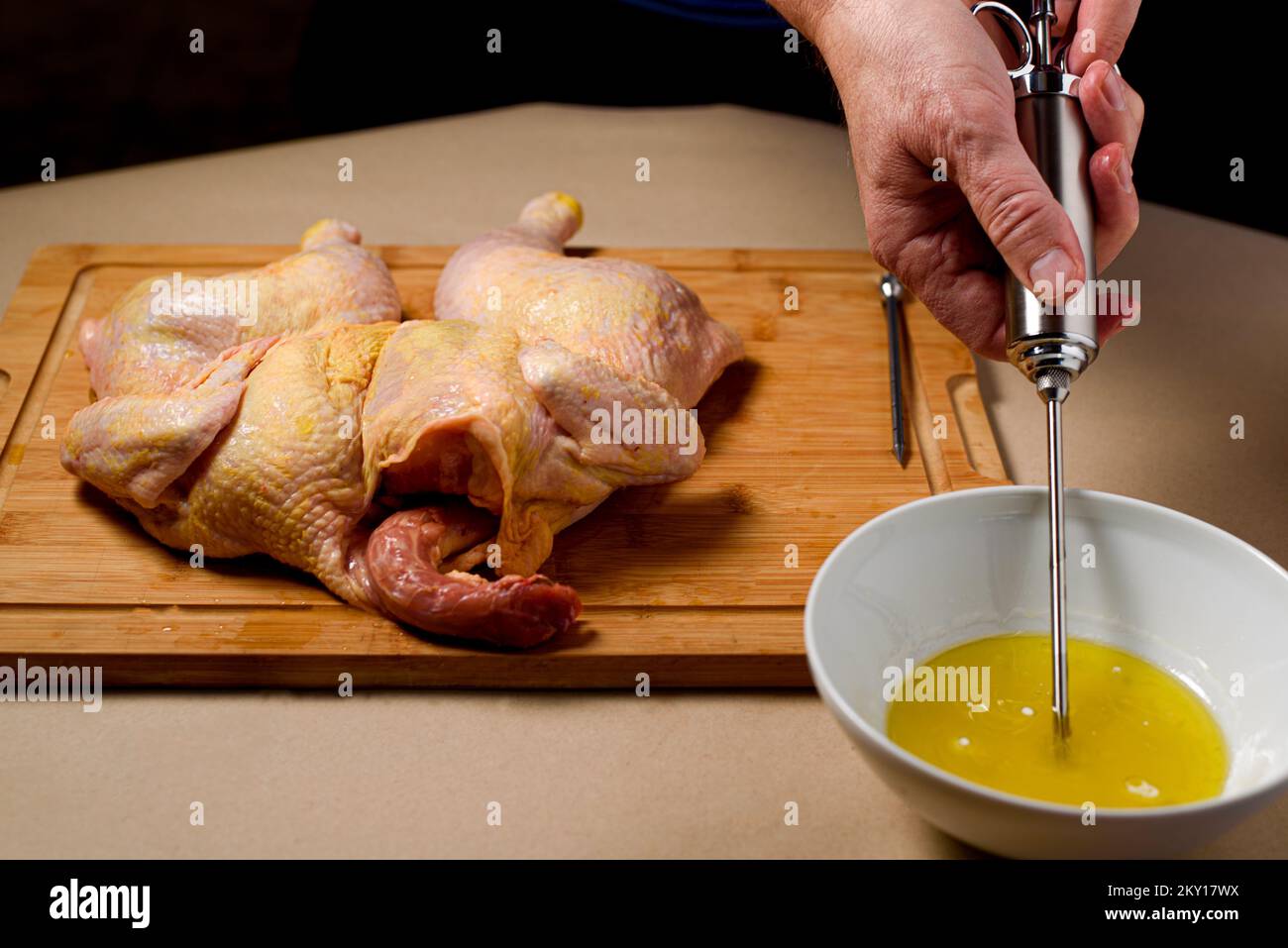 Der Küchenchef bereitet rohes Hähnchen in der Küche zu. Der Mensch bereitet rohes Hähnchen zum Grillen zu und injiziert dabei Cider in das Fleisch. Nahaufnahme. Stockfoto