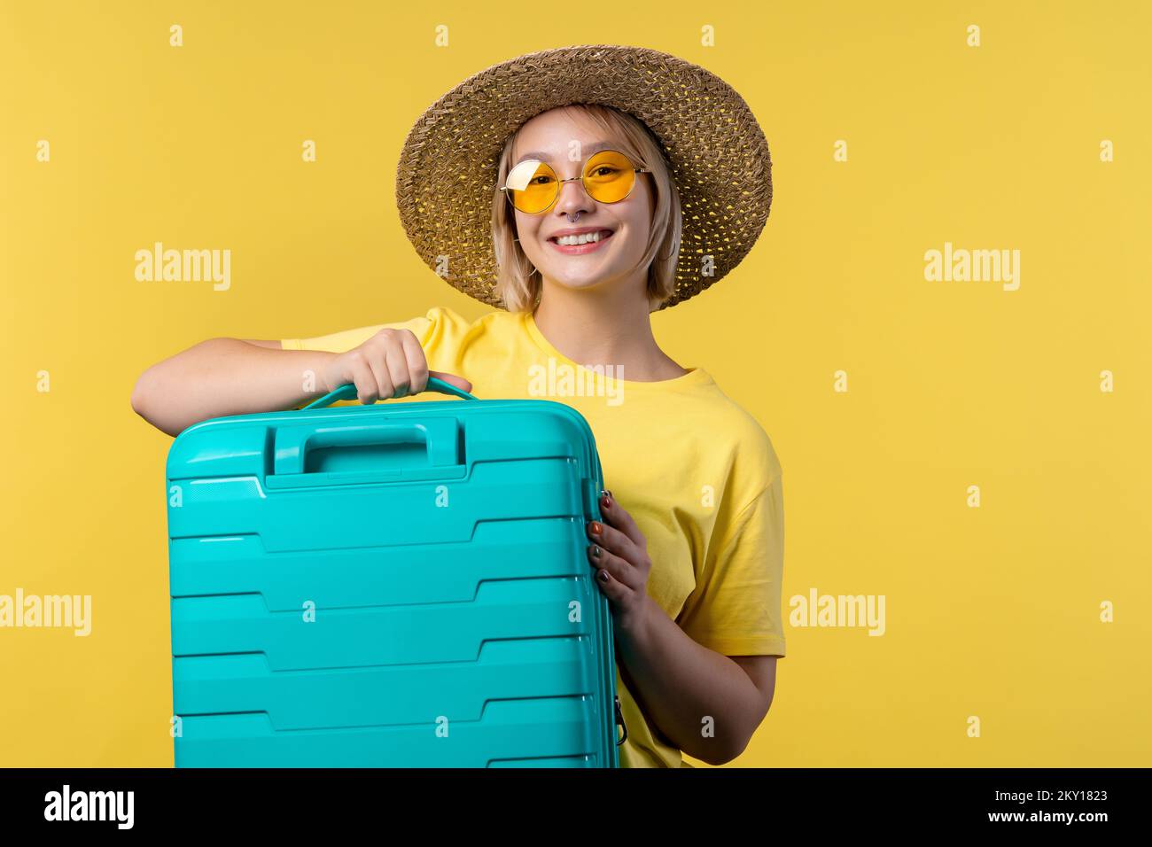 Junge hübsche Frau mit Handgepäckkoffer auf gelbem Hintergrund. Teenager, der mit blauer Gepäcktasche für das Handgepäck des Flugzeugs reist. Sommerreisen Stockfoto
