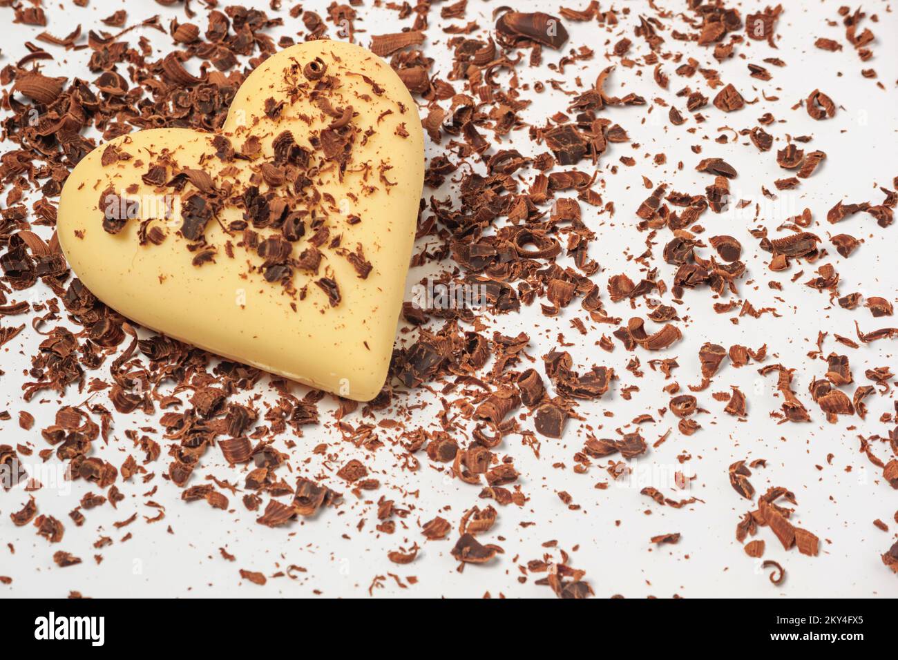 Blick auf ein weißes Schokoladenherz in Schokoladenchips auf weißem Hintergrund, Nahaufnahme. Valentinstagskonzept Stockfoto