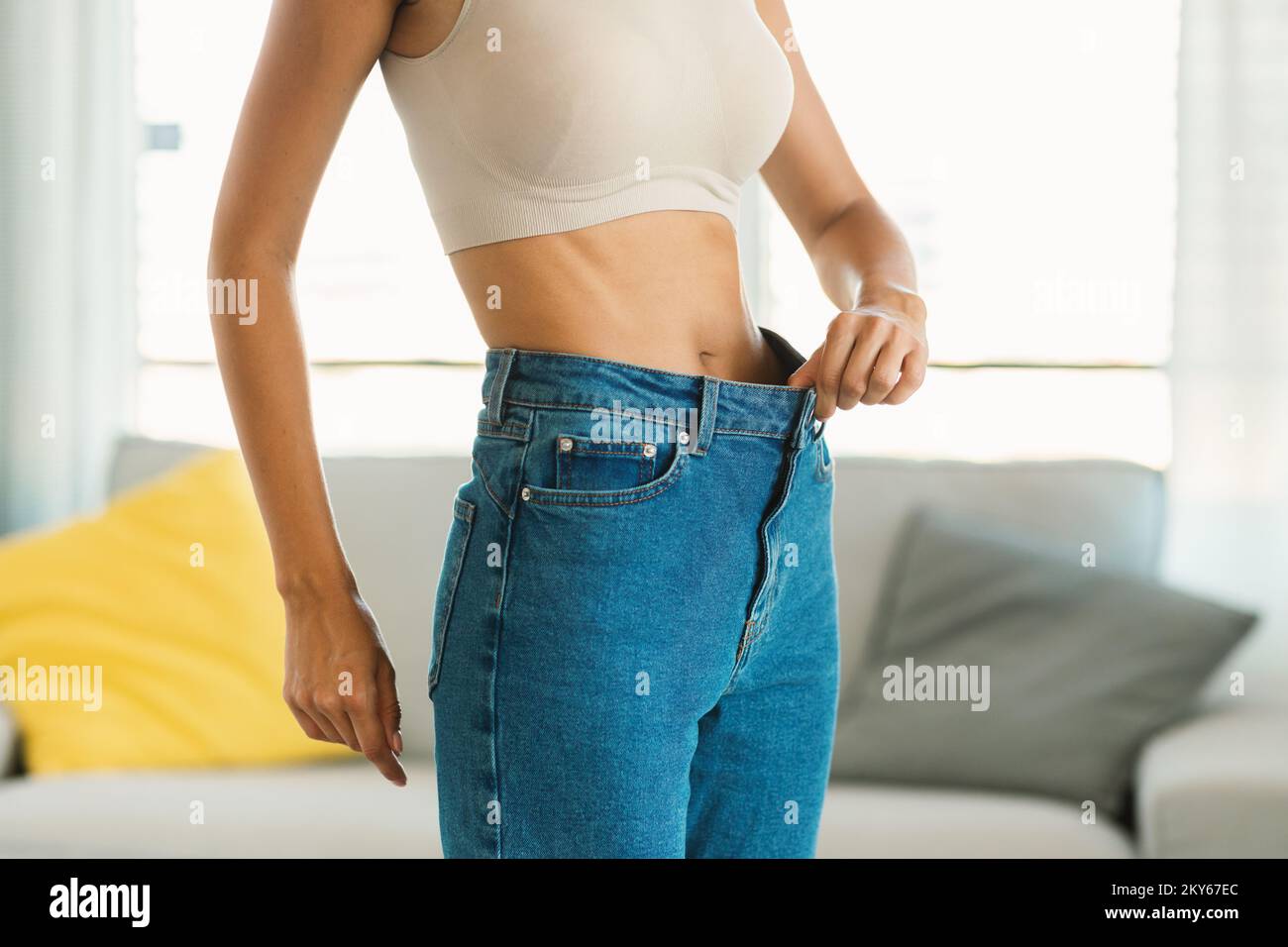 Schlanke junge Dame in zu großen Jeans zeigt, wie sie Gewicht verliert, gesunde Lebensmittel zu essen und trainieren, freier Platz Stockfoto