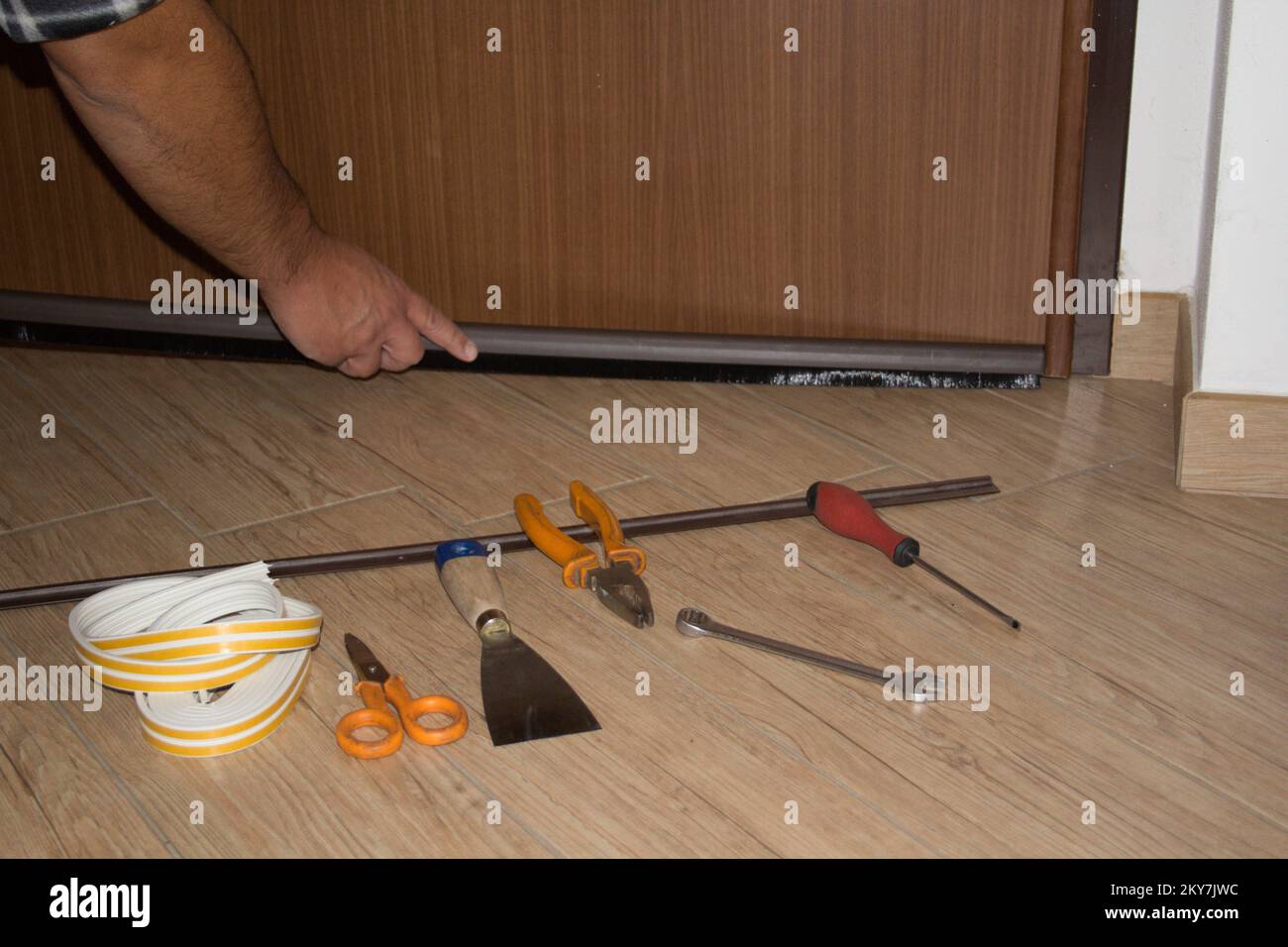 Handwerker, der eine Staubdichtung an der Haustür installiert. Bessere Wärmedämmung und Bodenreinigung. Horizontales Banner Stockfoto