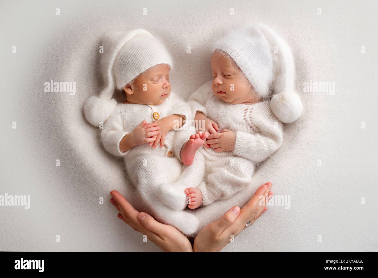 Winzige neugeborene Zwillingsjungen in weißen Bodys auf weißem Hintergrund. Stockfoto