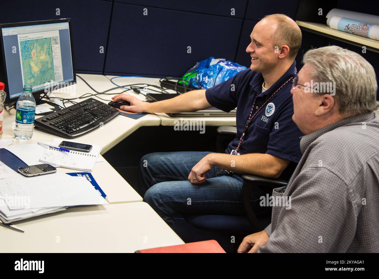 Warren, MI, 30. Oktober 2014 - Scott Bailey (Sitz, Betriebscomputer), FEMA Geographic Information System (GIS) Specialist demonstriert eine GIS Information Technology (IT)-Anwendung einem Vertreter des Macomb County Office of Emergency Management (OEM) im FEMA Joint Field Office (JFO) in Warren, Michigan nach den schweren Stürmen und Überschwemmungen vom 11. Bis 13. August 2014, die die Michigan Grafschaften Wayne, Oakland und Macomb negativ beeinflussten. Die FEMA unterstützt lokale und staatliche Regierungen und Stammeseinheiten bei ihren Bemühungen, sich von Naturkatastrophen zu erholen. Michigan, schwere Stürme und Stockfoto