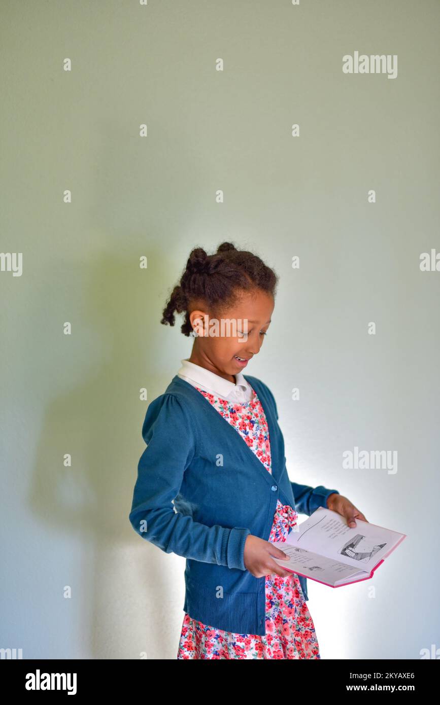 Ein kleines Mädchen, das aufsteht und ein Buch für die Schule liest Stockfoto