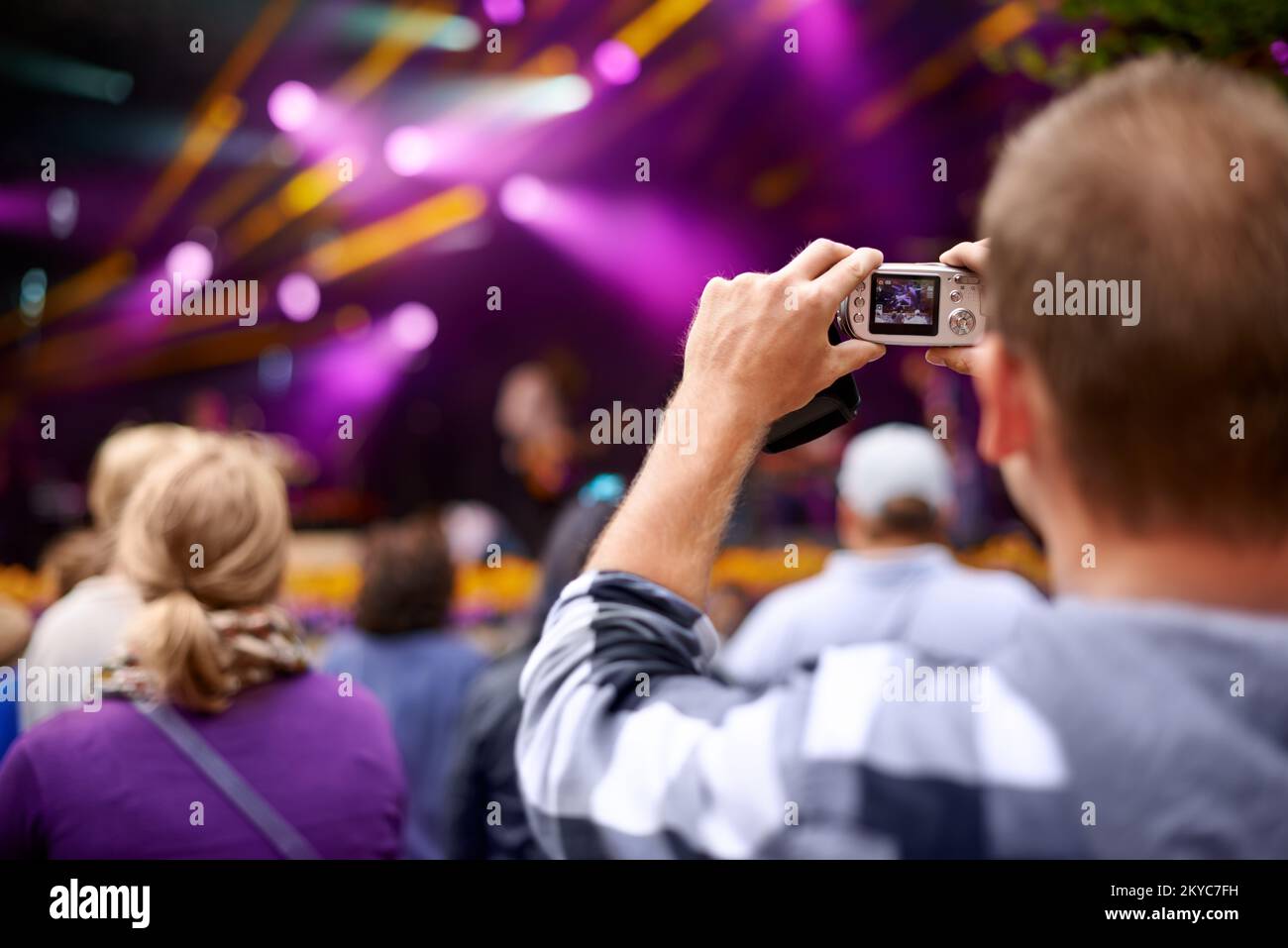 Leben mit Verschlusszeit. Rückansicht eines Mannes in der Menge, der eine Kamera hält, um ein Konzert zu fotografieren. Stockfoto