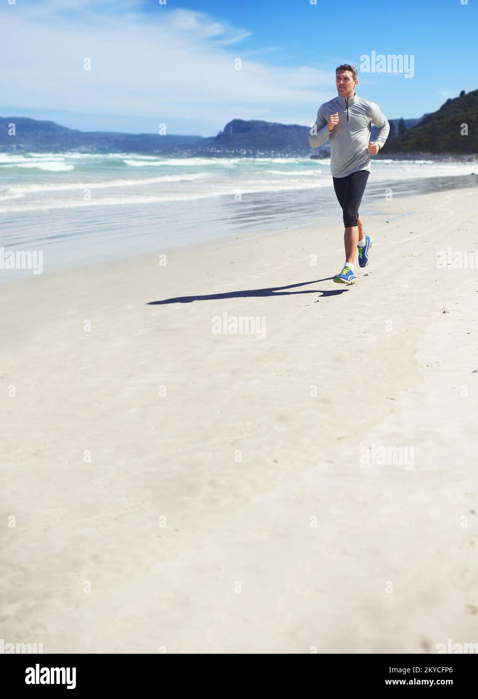 Fitness-Fanatiker. Die ganze Länge eines Mannes, der am Strand joggt. Stockfoto