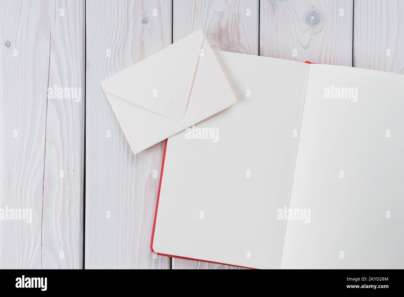 Rotes Tagebuch mit weißem Papier mit handgefertigtem Umschlag auf hellem Holzhintergrund. Traditionelles Versenden von Nachrichten, Postkarten für Stockfoto