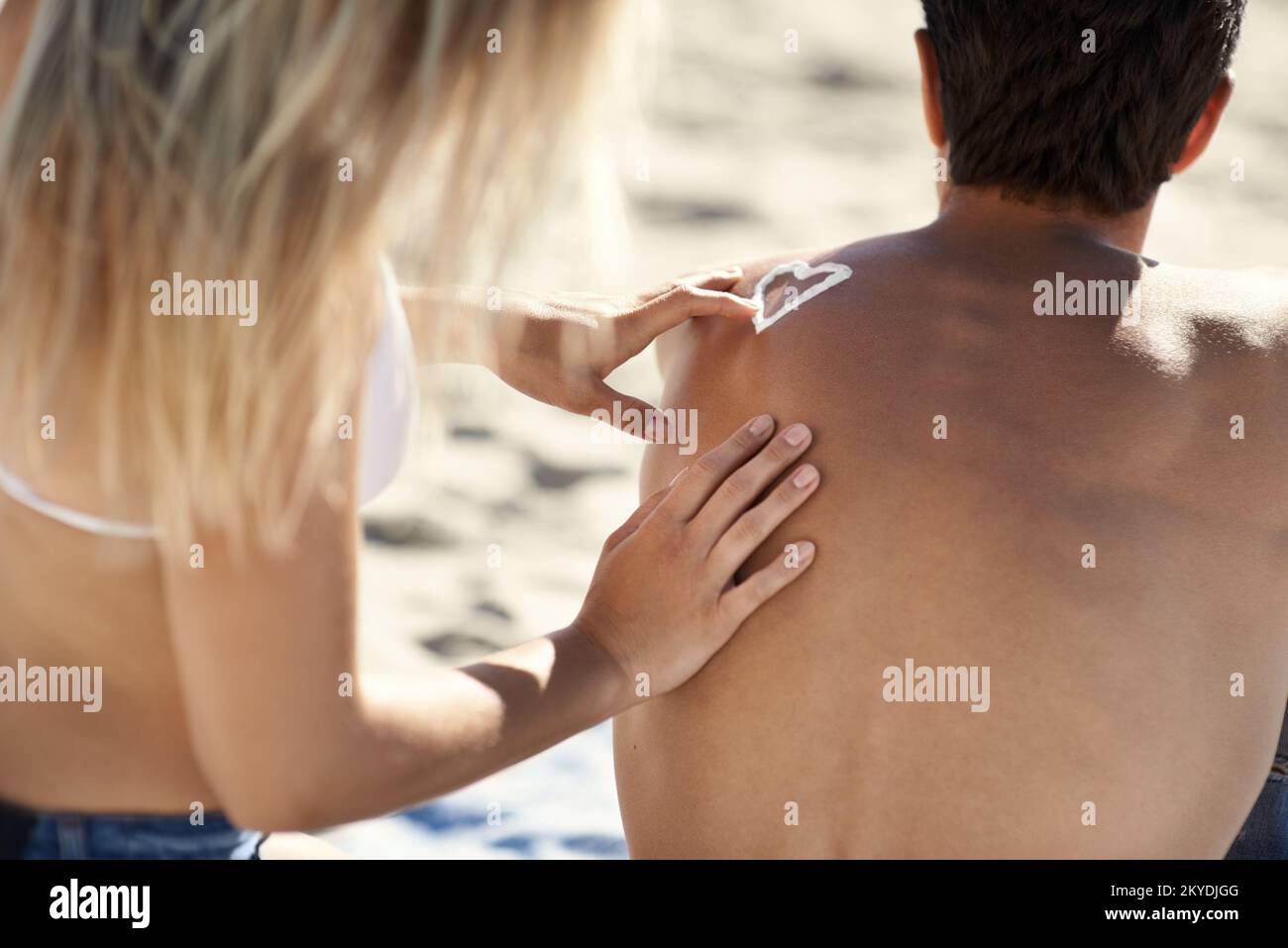 Der Sommer ist endlich da. Eine junge Frau, die ein Herz mit Sonnencreme auf dem Rücken ihres Freundes formt. Stockfoto
