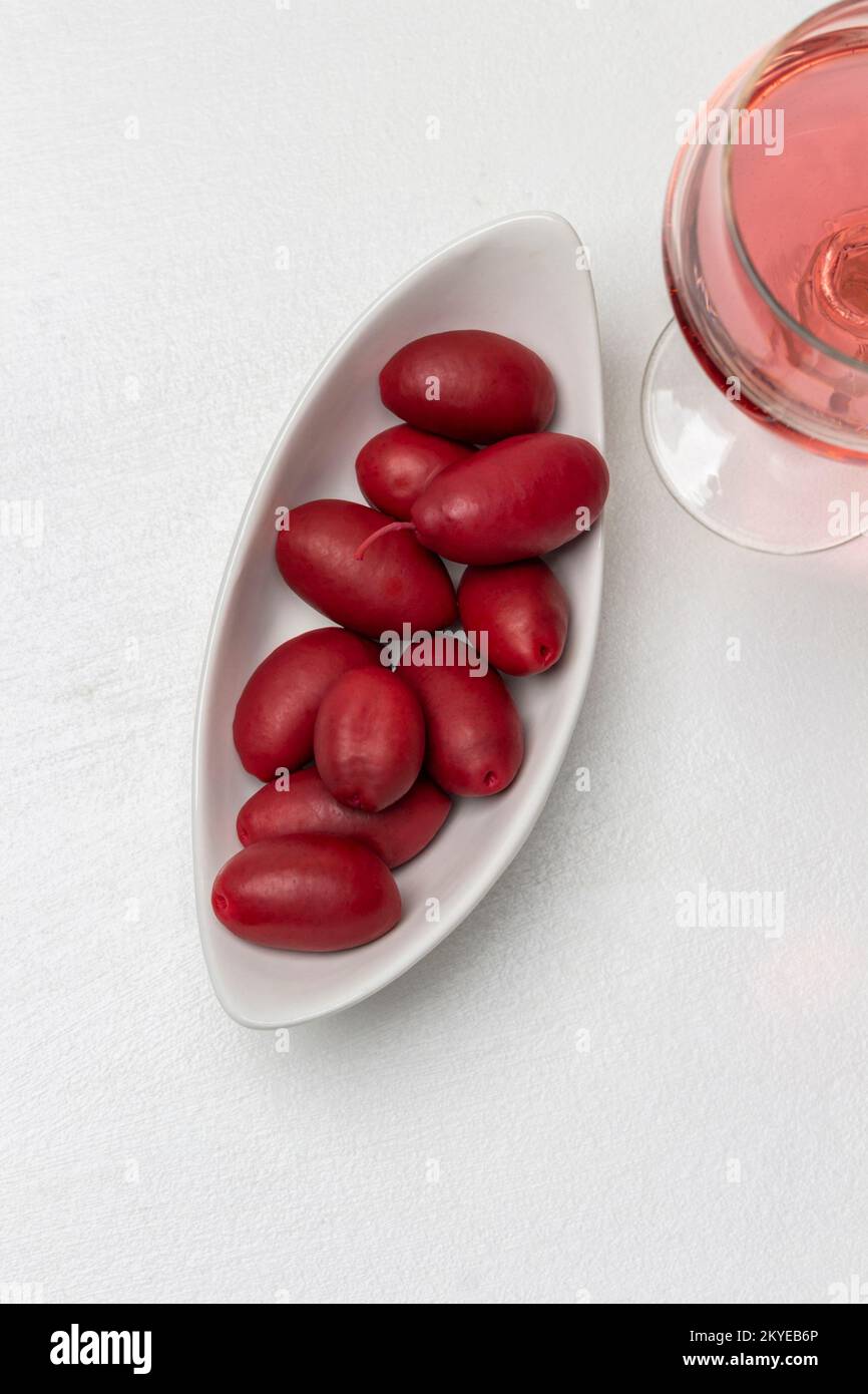 Rote Oliven in einer weißen Schüssel, ein Glas Rotwein. Weißer Hintergrund. Speicherplatz kopieren. Flach verlegt. Stockfoto