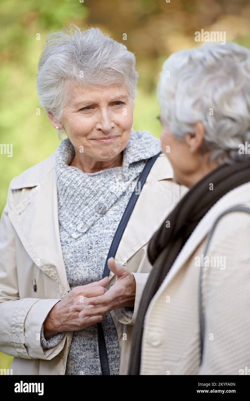 Ein freundliches Ohr zu schenken. Ältere Frauen lächeln und hören einem Freund zu. Stockfoto