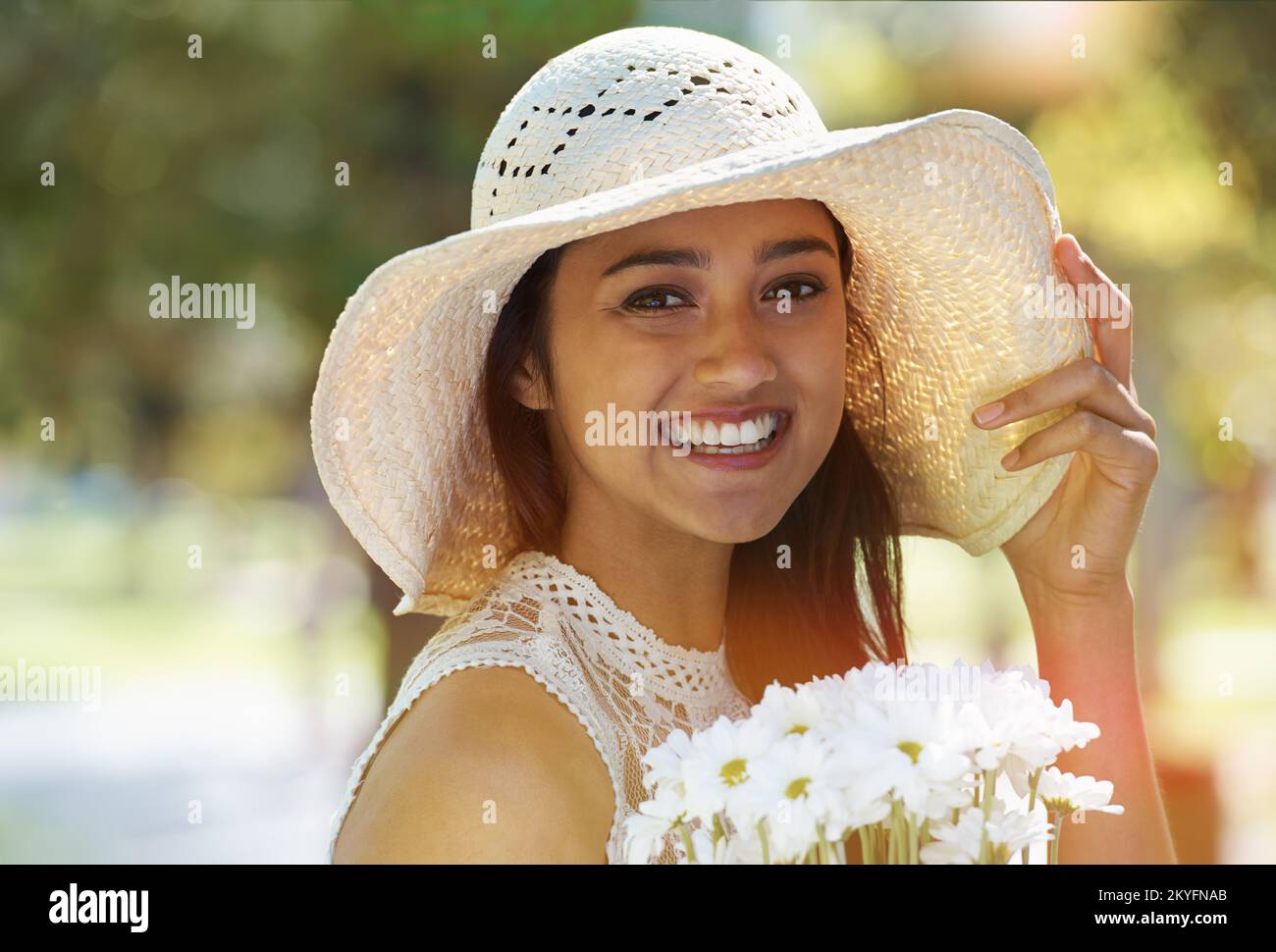Der Frühling ist da. Eine junge Frau, die Blumen in der Hand hält und einen Sonnenhut trägt, während sie in einem Park steht. Stockfoto