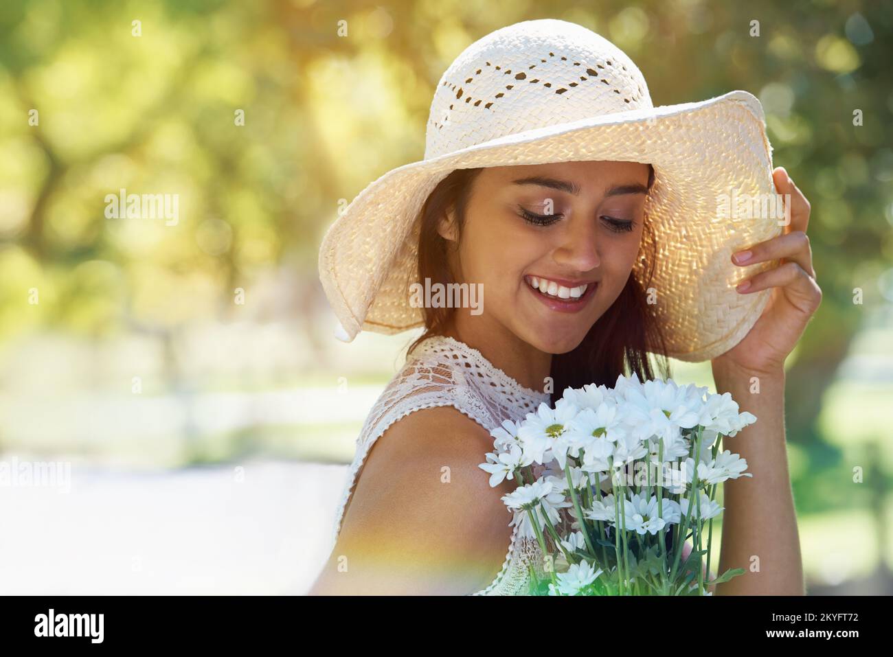 Der Frühling ist da. Eine junge Frau, die Blumen in der Hand hält und einen Sonnenhut trägt, während sie in einem Park steht. Stockfoto