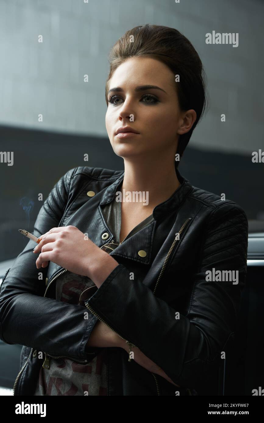 Eine rebellisch aussehende junge Frau, die in einer Garage eine Zigarette raucht. Stockfoto