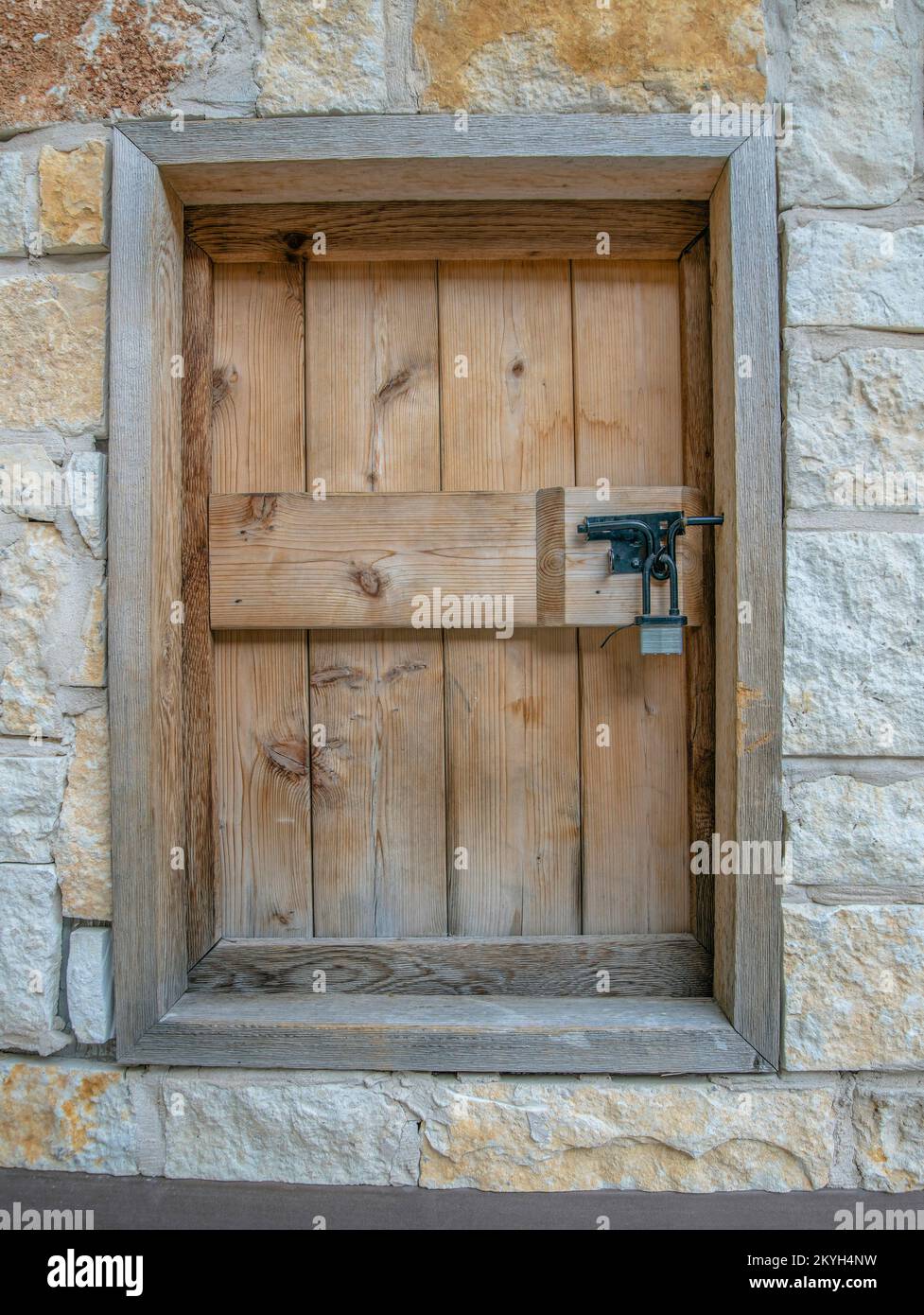 San Antonio, Texas – Holzvorhänge mit Vorhängeschloss. Kleine Fensternahaufnahme mit Holzabdeckung und Rahmen in der Mitte rauer Steinwände. Stockfoto