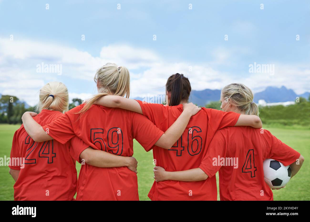 Bereit, das Feld zu übernehmen. Eine Fußballmannschaft der Mädchen, die mit ihren Armen um die Schultern herum steht und auf das Spielfeld blickt. Stockfoto