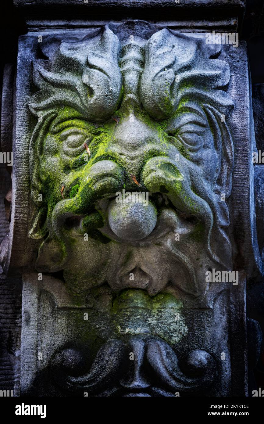 Monstergesicht mit Löwenmähne und Schnurrbart, gruselige verwitterte Steinskulptur mit Moos, Fantasy Kreatur Steinwerk Dekoration auf einer Veranda Stockfoto